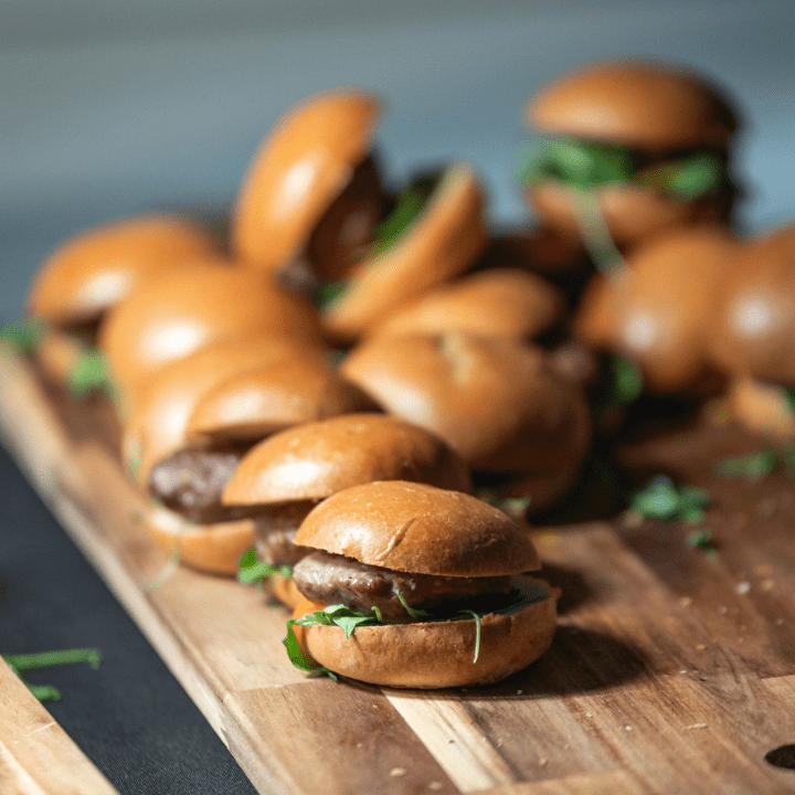 Corporate event catering of mini burgers on a wooden board.